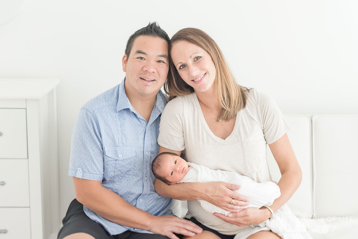 happy couple holding their newborn baby boy while sitting on a couch