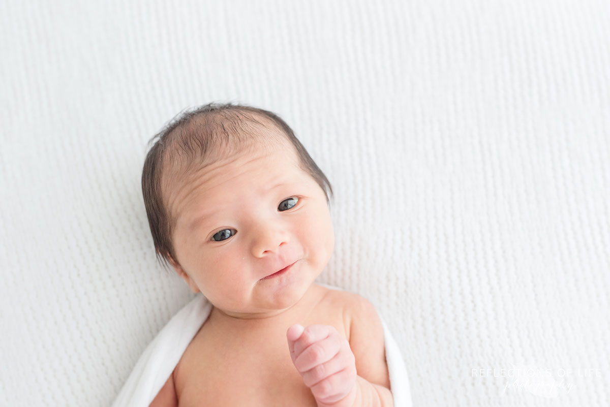 newborn boy holding hand out in front of him smiling while laying down