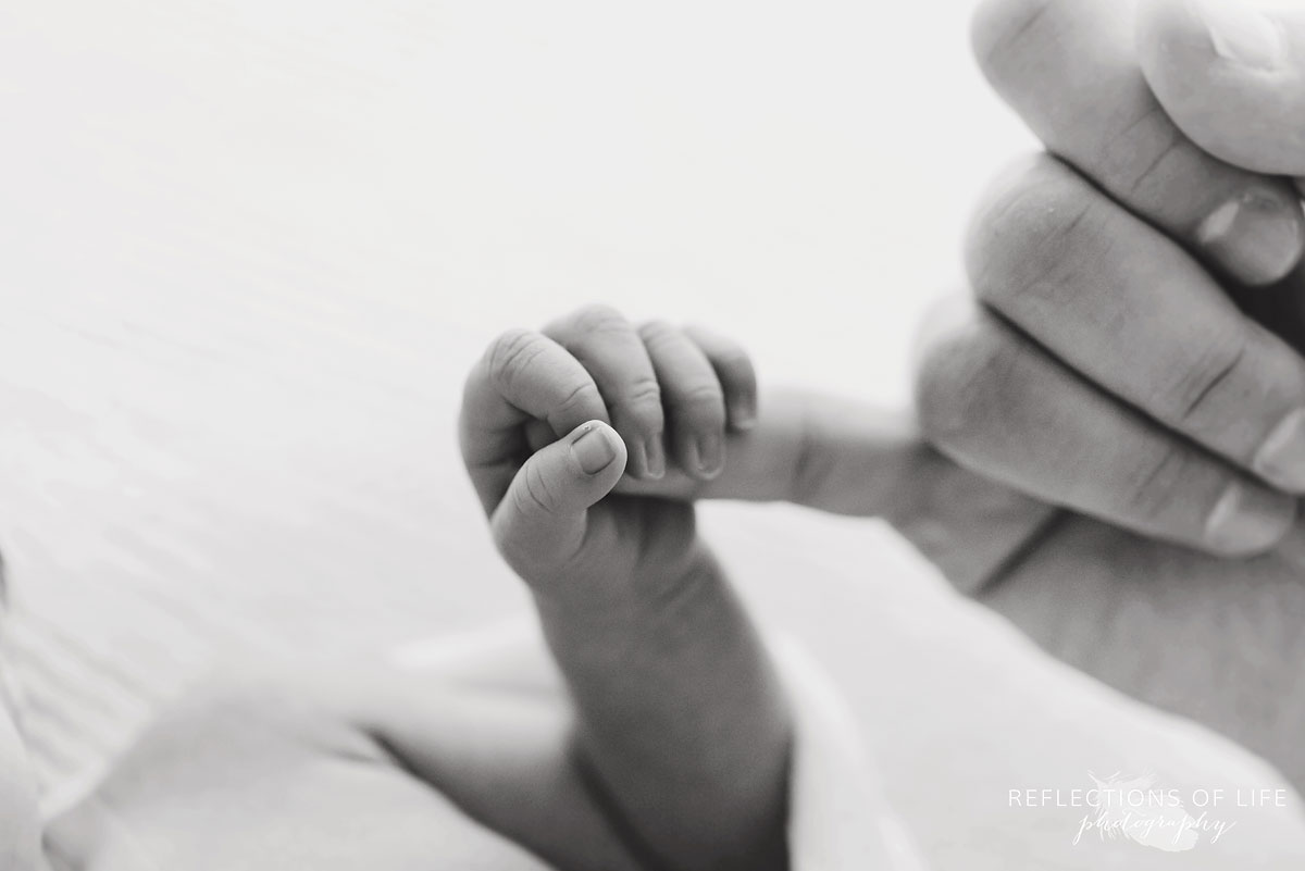 newborn baby holding father's pinkie finger black and white