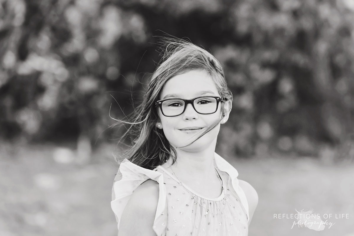 black and white of young girl with glasses smiling at camera