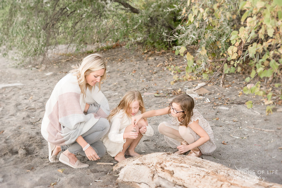 mother and daughters looking at rocks on beach