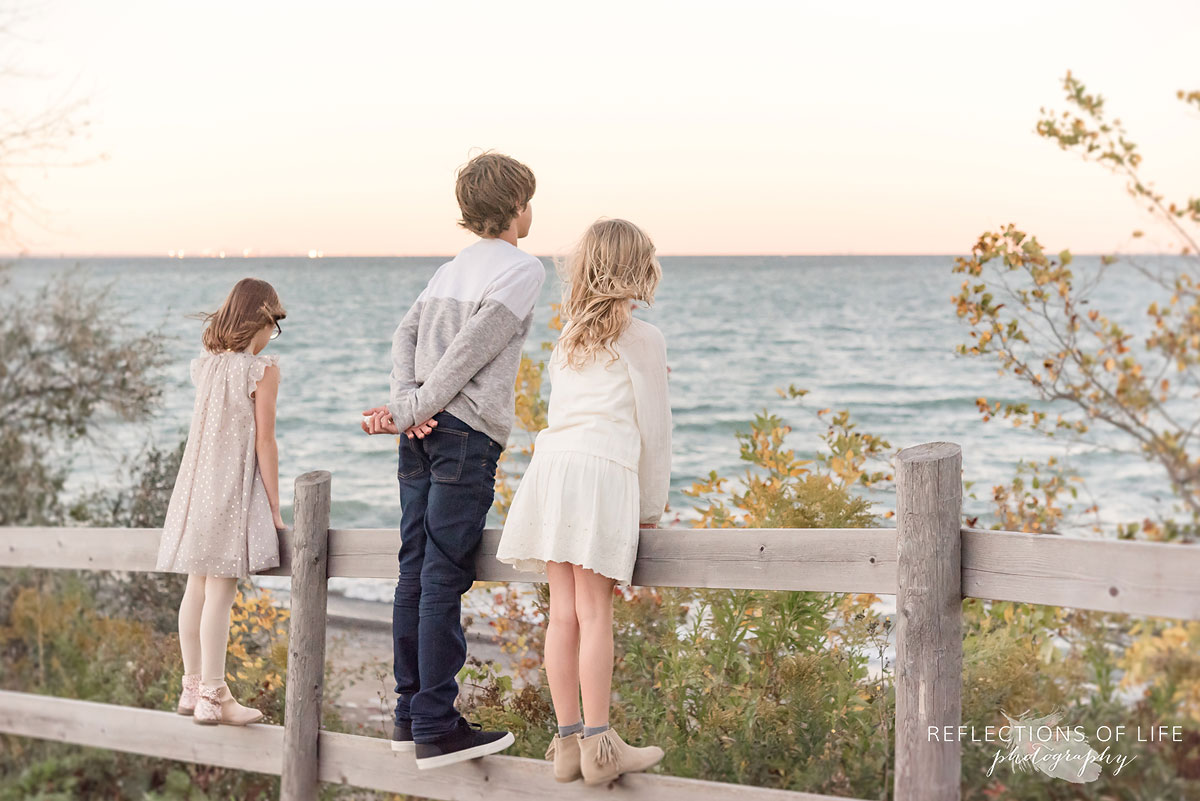 three sibling looking out at beach by wooden fence