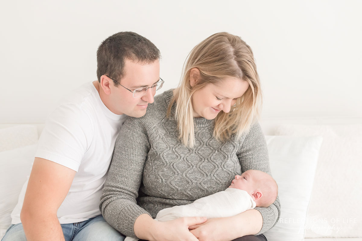 husband and wife on white couch with newborn