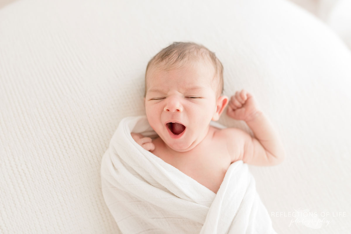 newborn baby yawning with fist