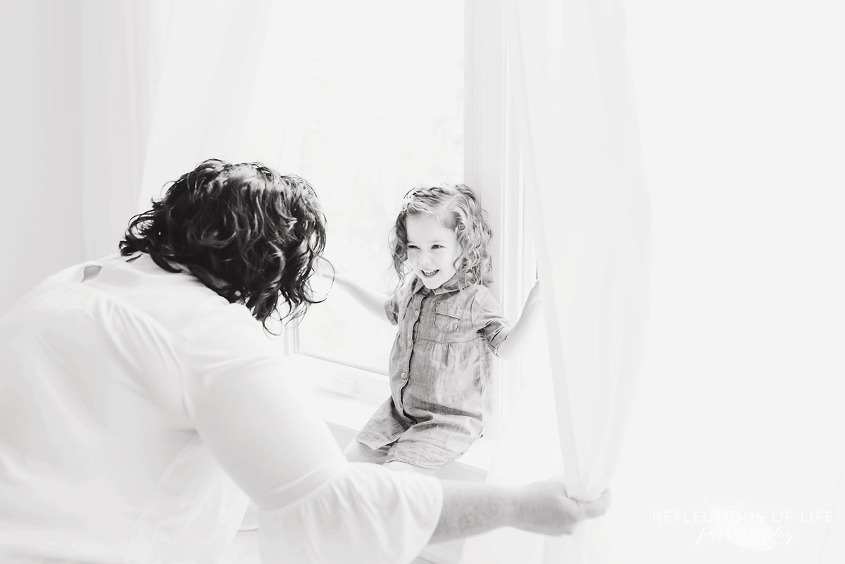 mom opening curtains to daughter black and white