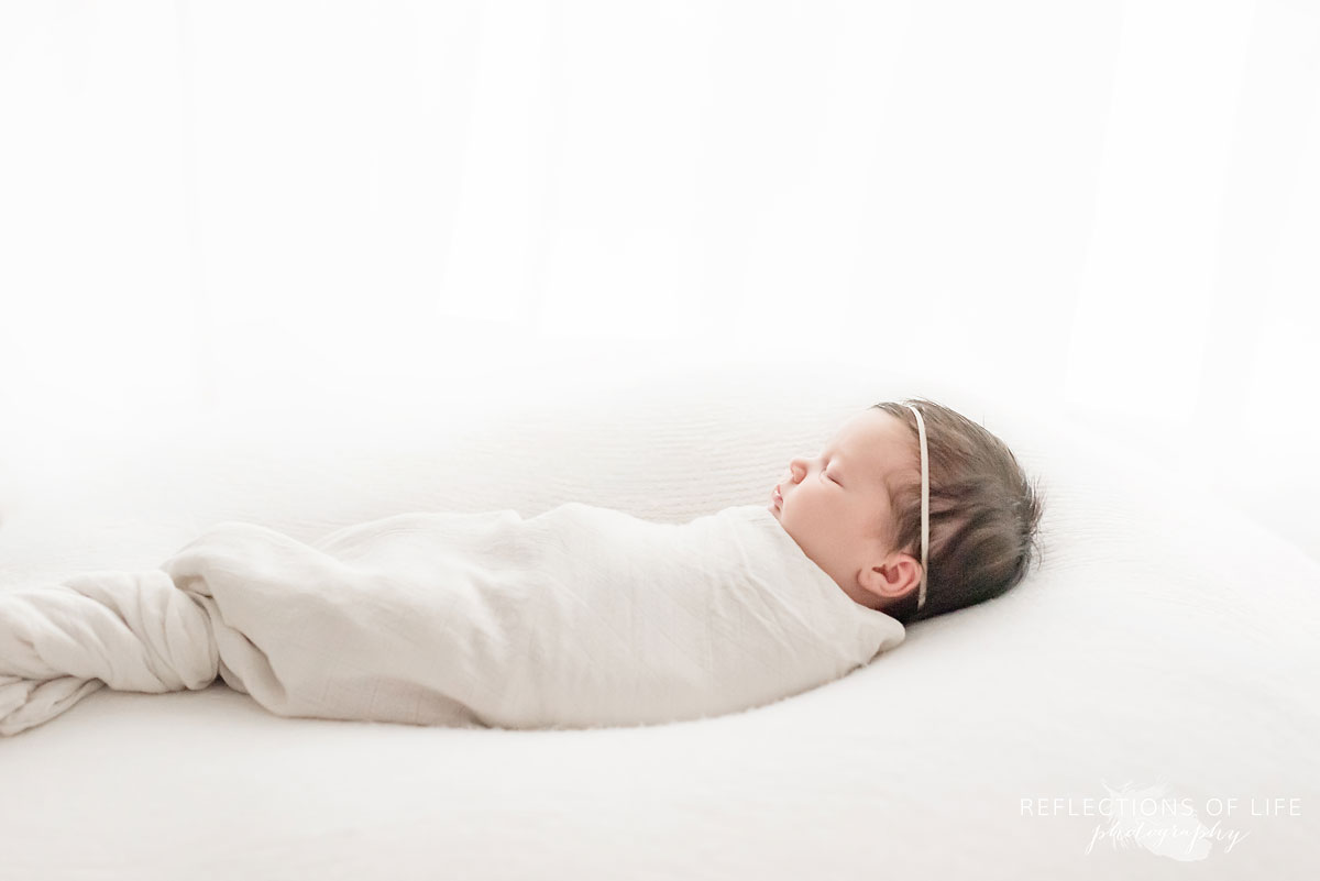newborn baby girl swaddled in white on a white bed.jpg