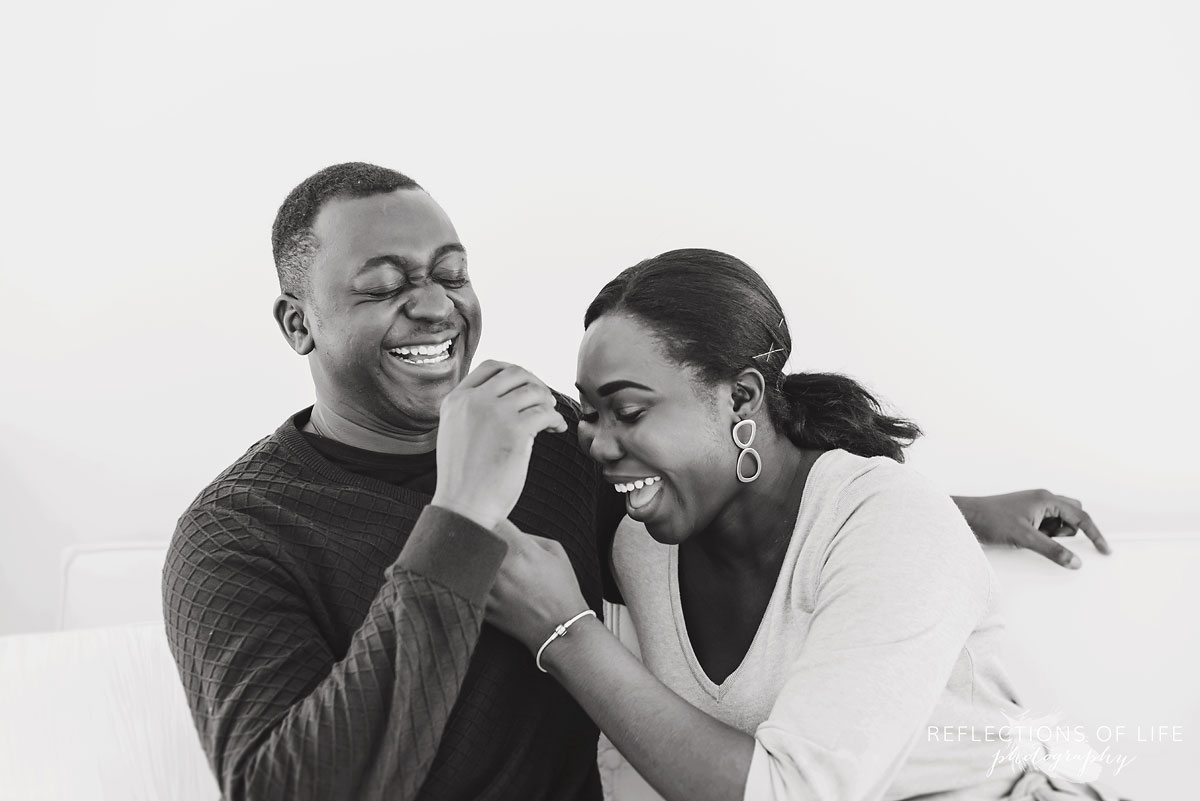 New mom and dad couple laughing together on a couch in the studio