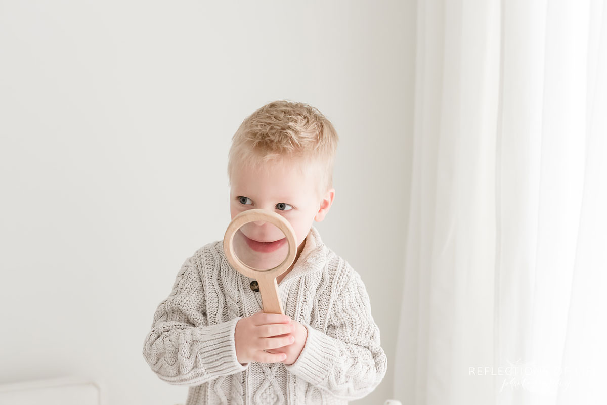 Fun portrait of little boy making his mouth larger with a magnifying glass.jpg