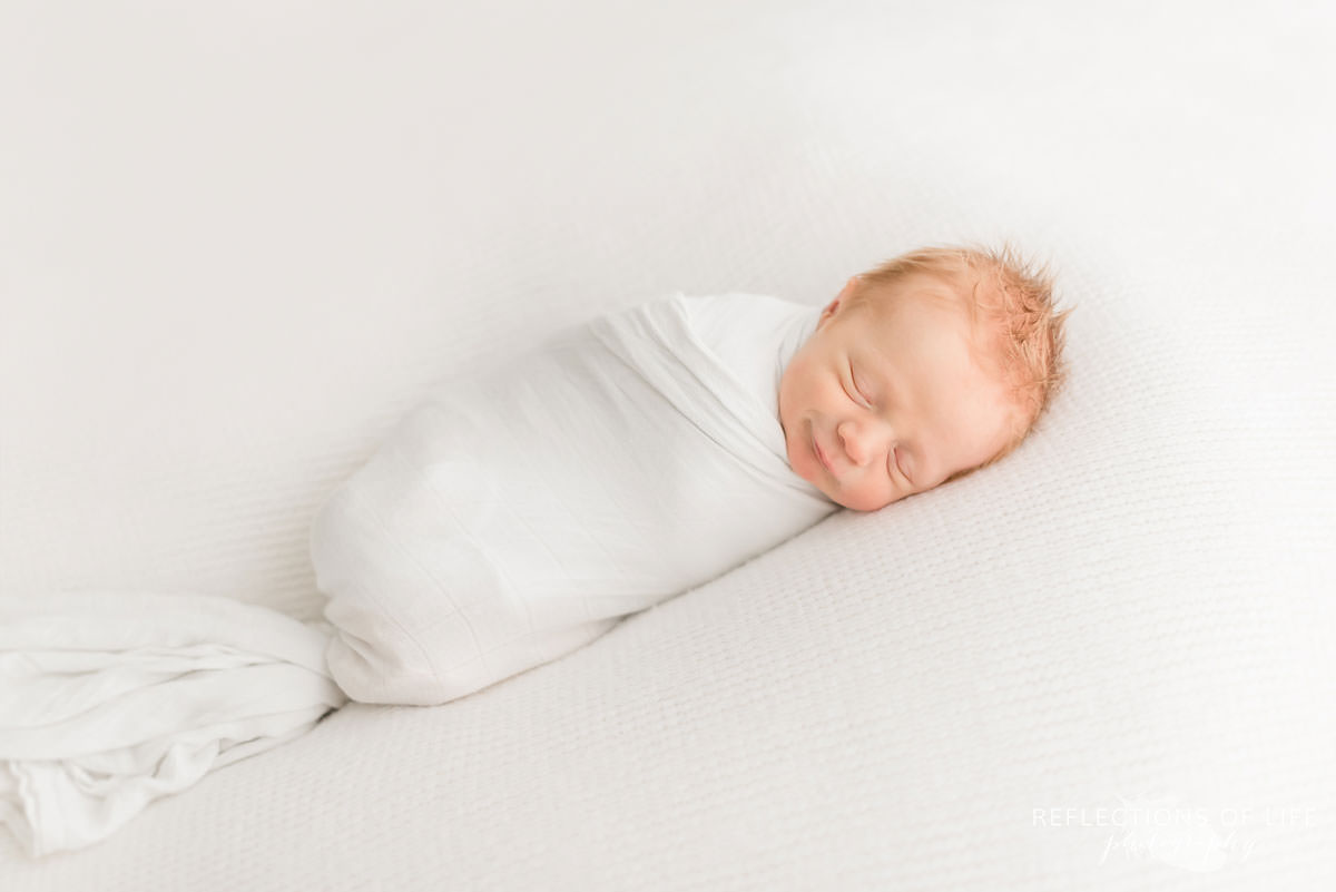 Newborn baby boy swaddled in white and sleeping.jpg