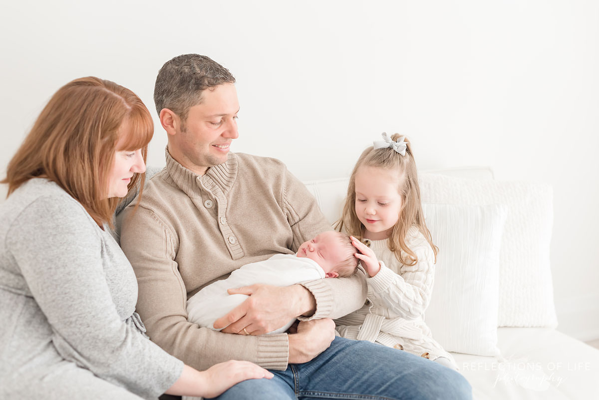 family of four looks at newborn sister touches its head