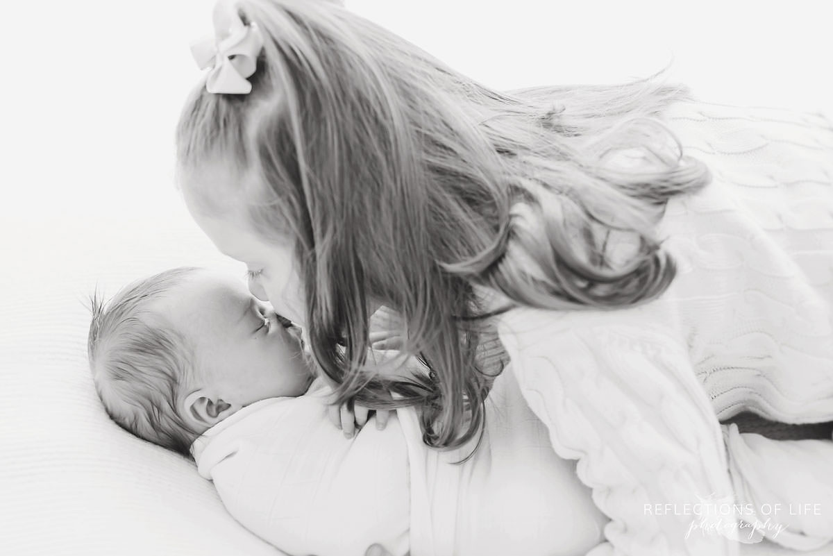 two siblings sister leans over to kiss baby