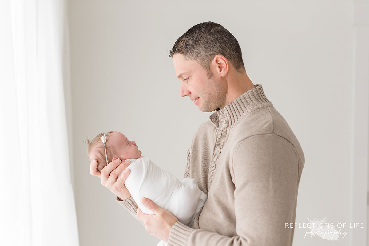 Father looks at sleeping baby profile in natural light studio