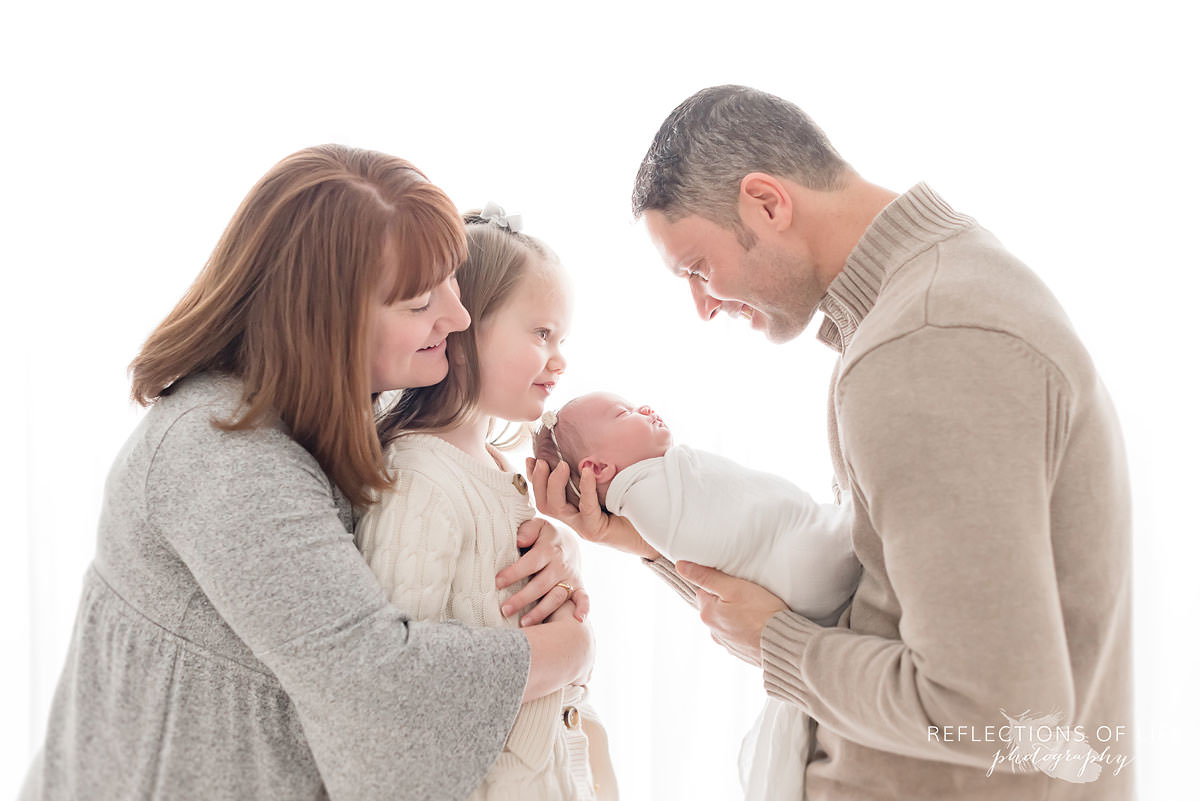 Family of four smiles at sleeping baby in natural light studio