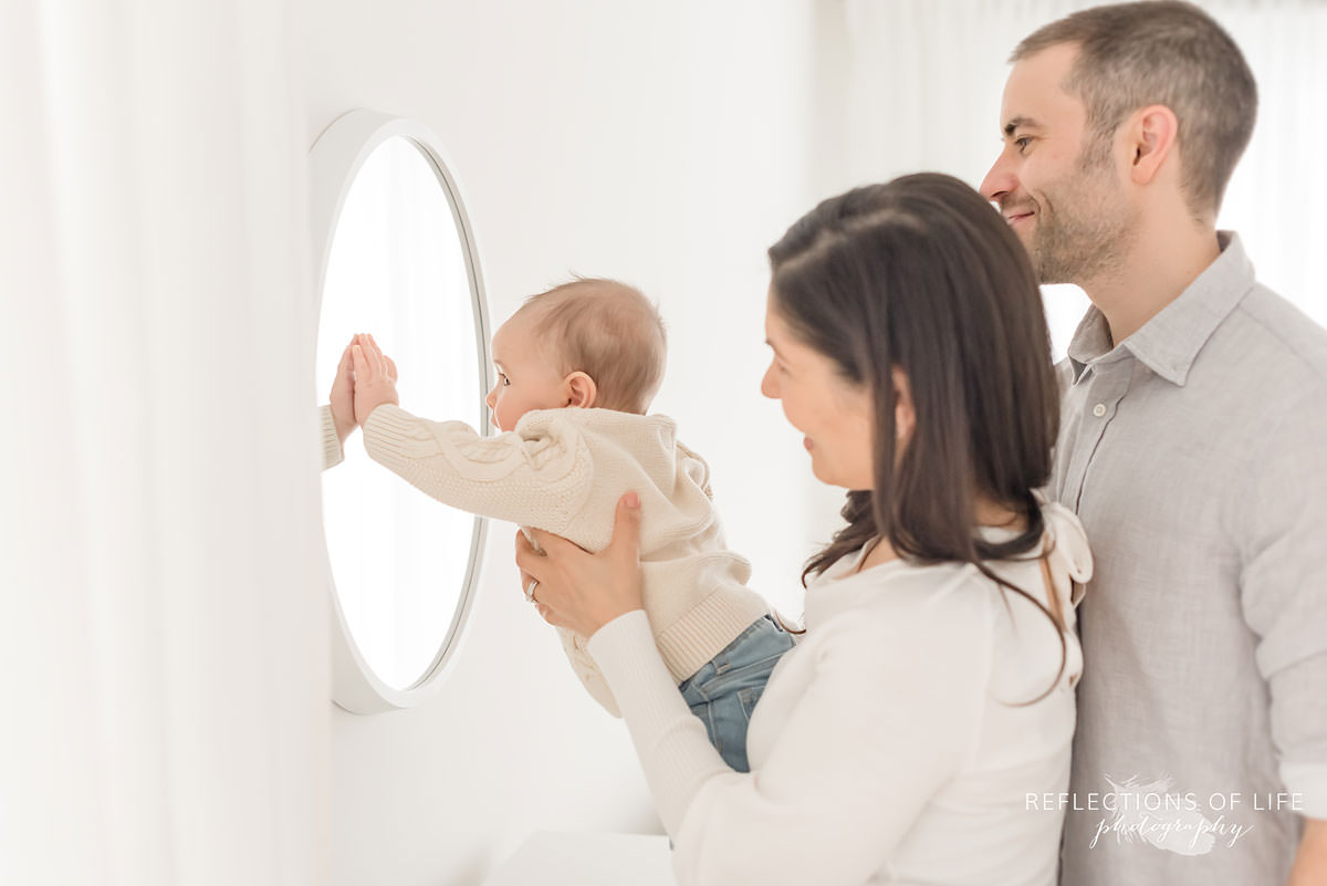 mother holds baby while he touches the mirror in ontario