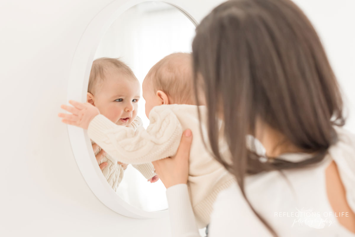 baby looks at himself in mirror in natural light studio
