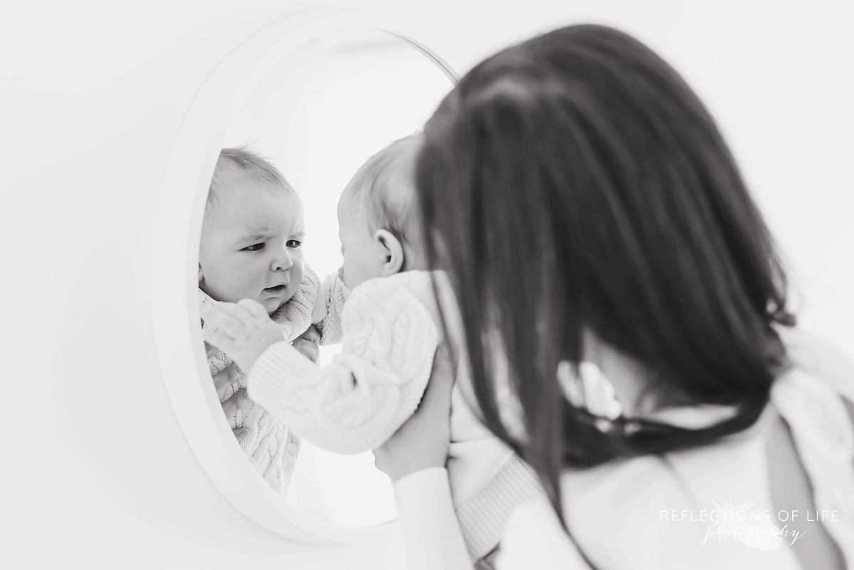 baby looks at himself in natural light studio in black and white