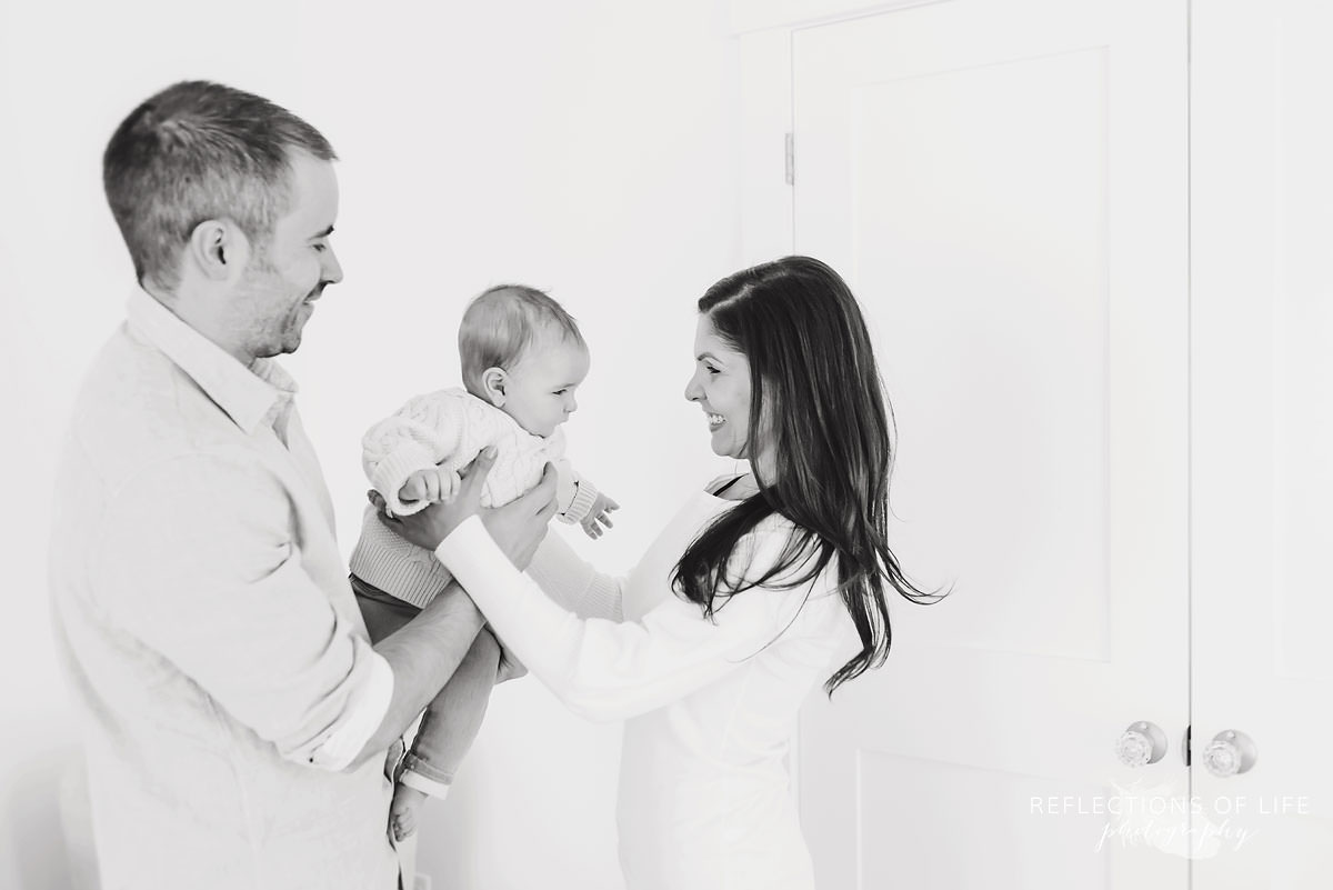 father passes baby off to mother as they smile in black and white