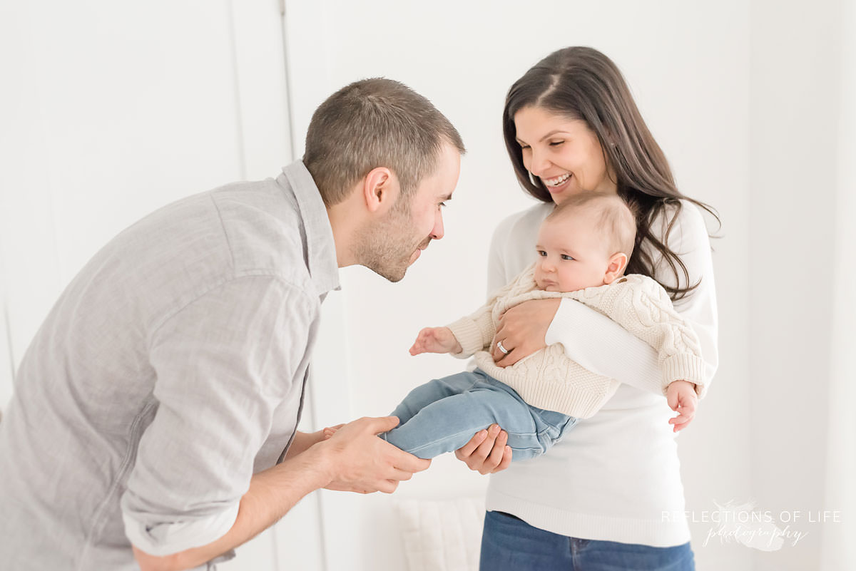 dad plays with baby's feet as mother holds him and laughs in ontario