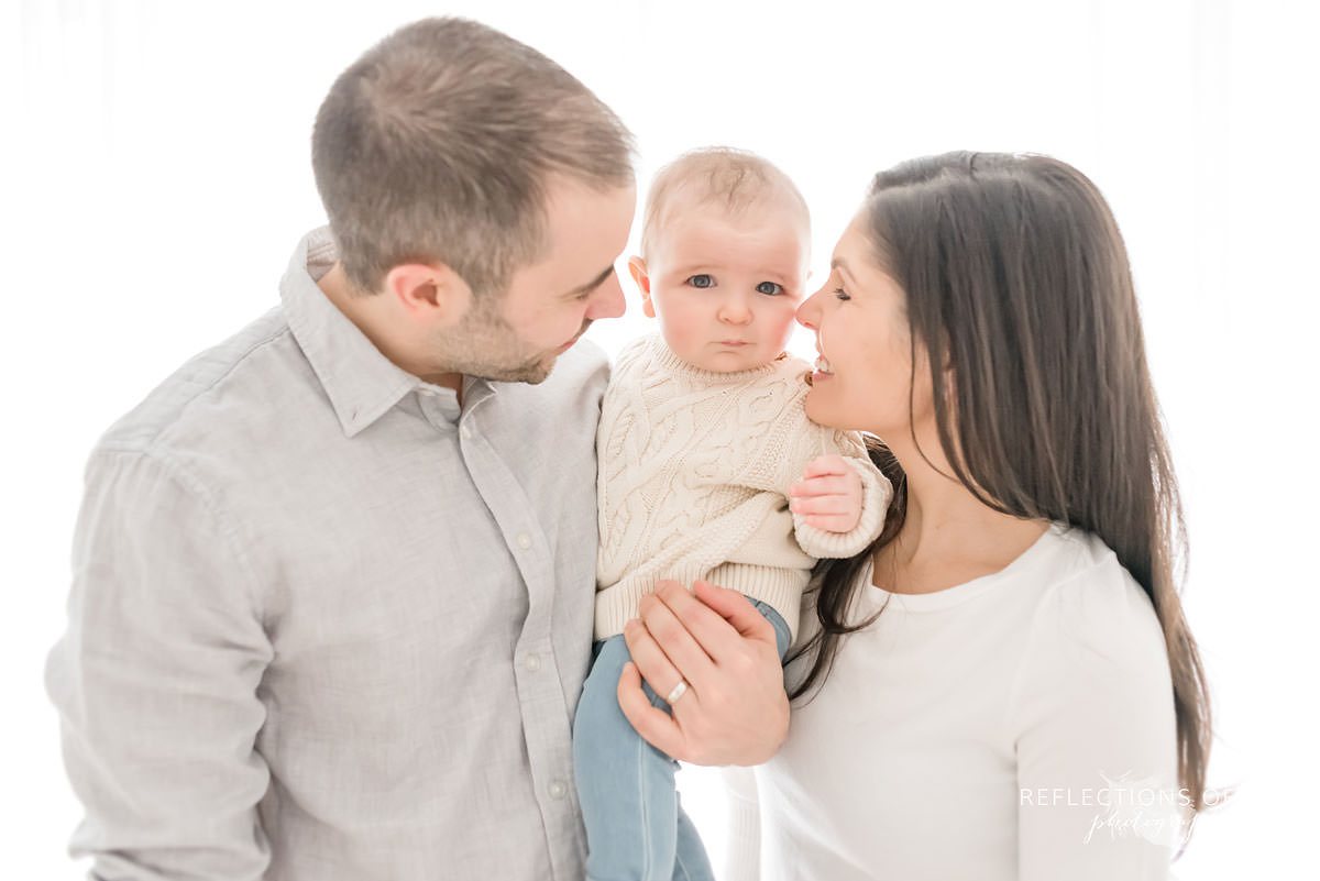 mom and dad admire baby as baby looks at camera in natural light studio