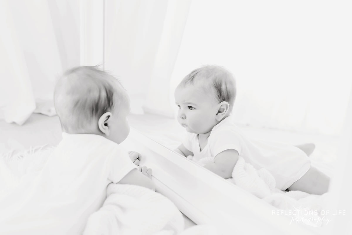 baby looks at himself in mirror in black and white