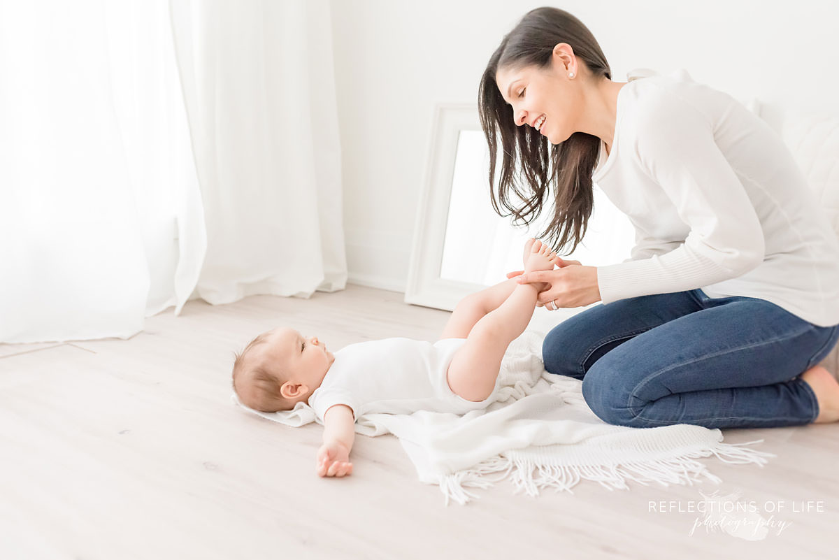 mom plays with baby's feet on floor in natural light studio