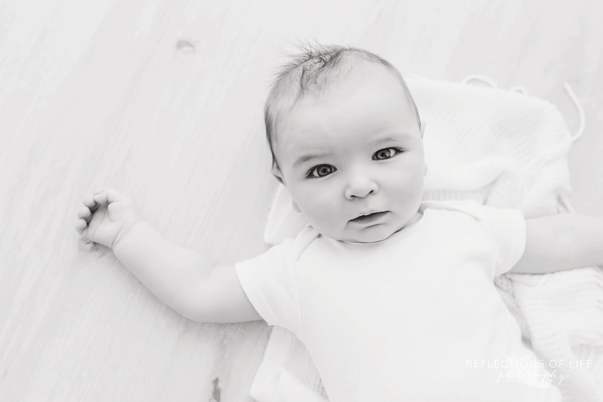 baby lays on ground holding up his head in black and white