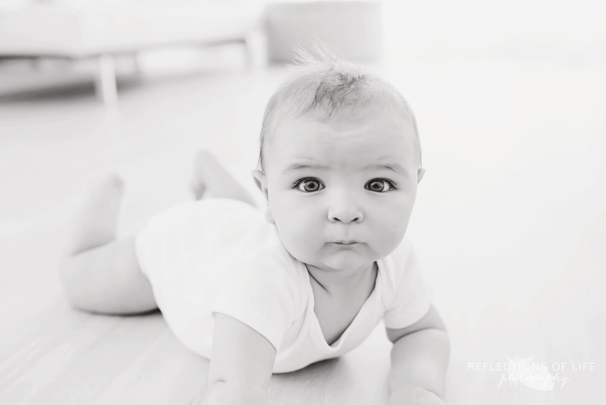 baby lays on the ground looking straight ahead in black and white