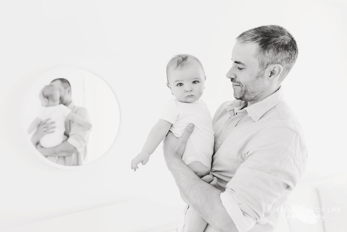 father holds son with reflection of them in the mirror in black and white