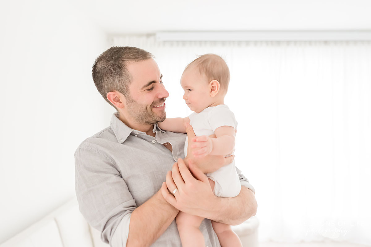 dad holds son as he smiles at him in natural light studio