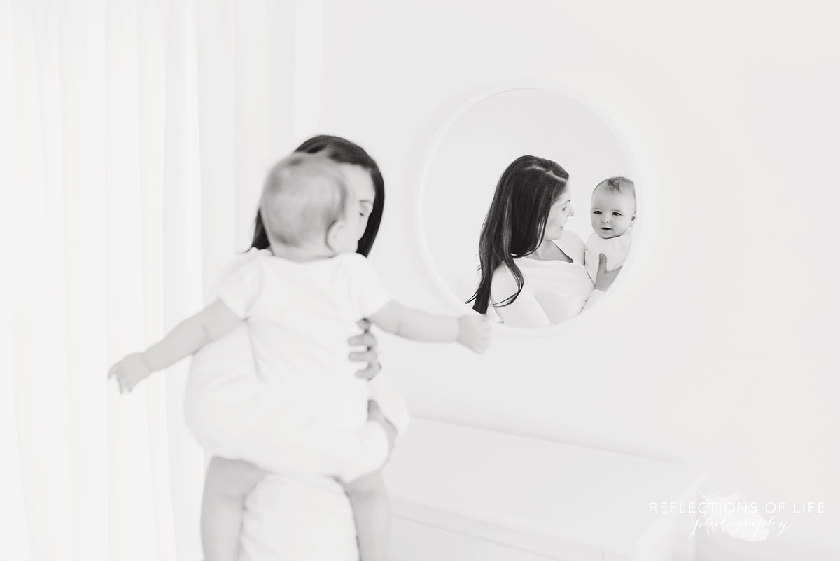 mother looks at baby as he looks at the mirror in black and white