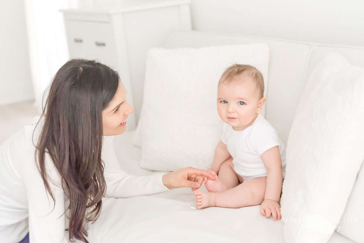 mother plays with baby's toes in natural light studio