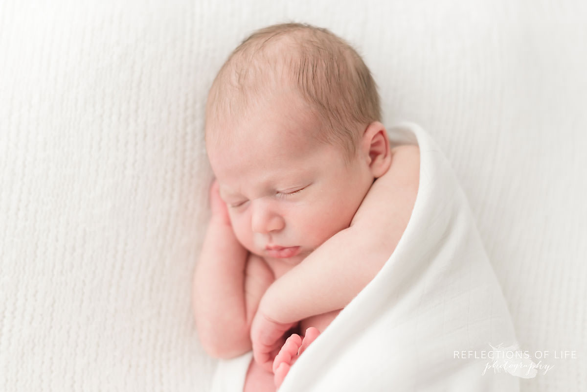 sleeping baby is snug in white blanket