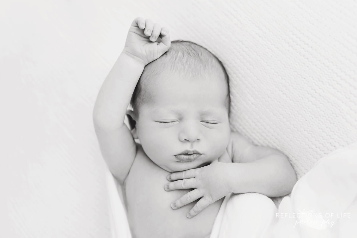 baby stretches out while it sleeps in black and white