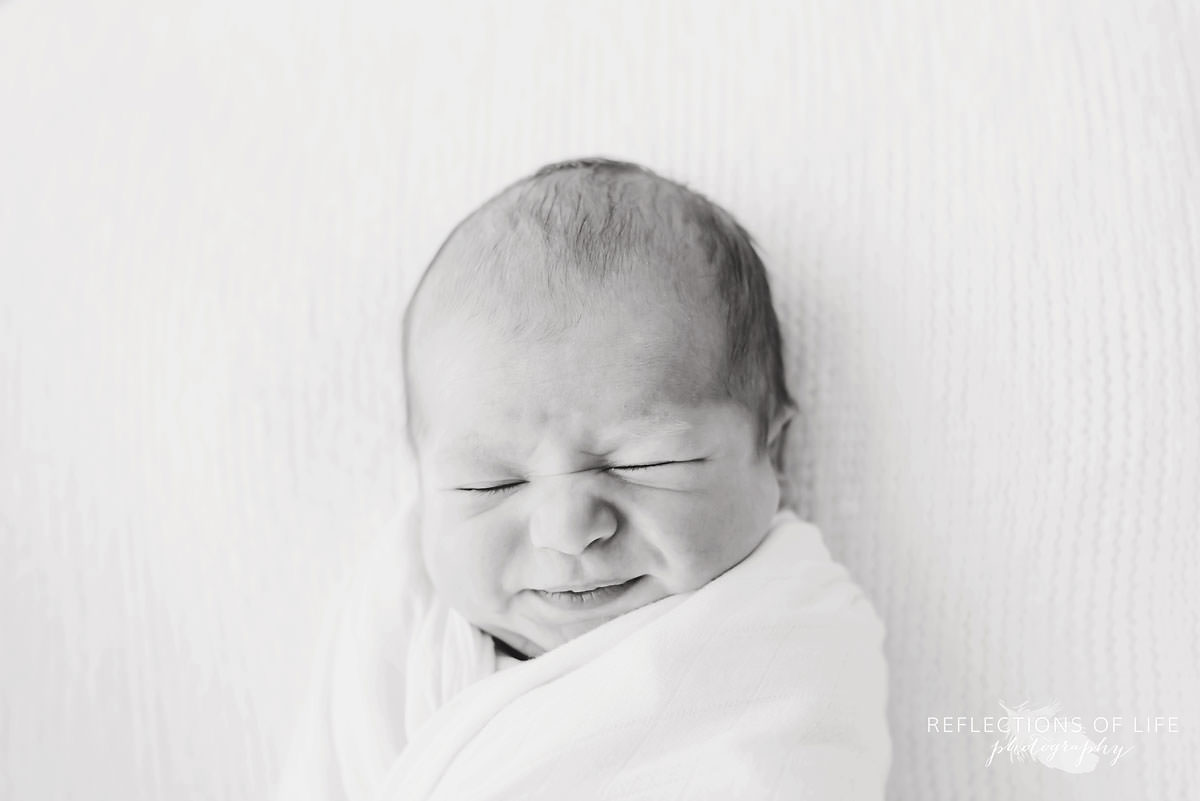 swaddled baby scrunches up it's face in black and white