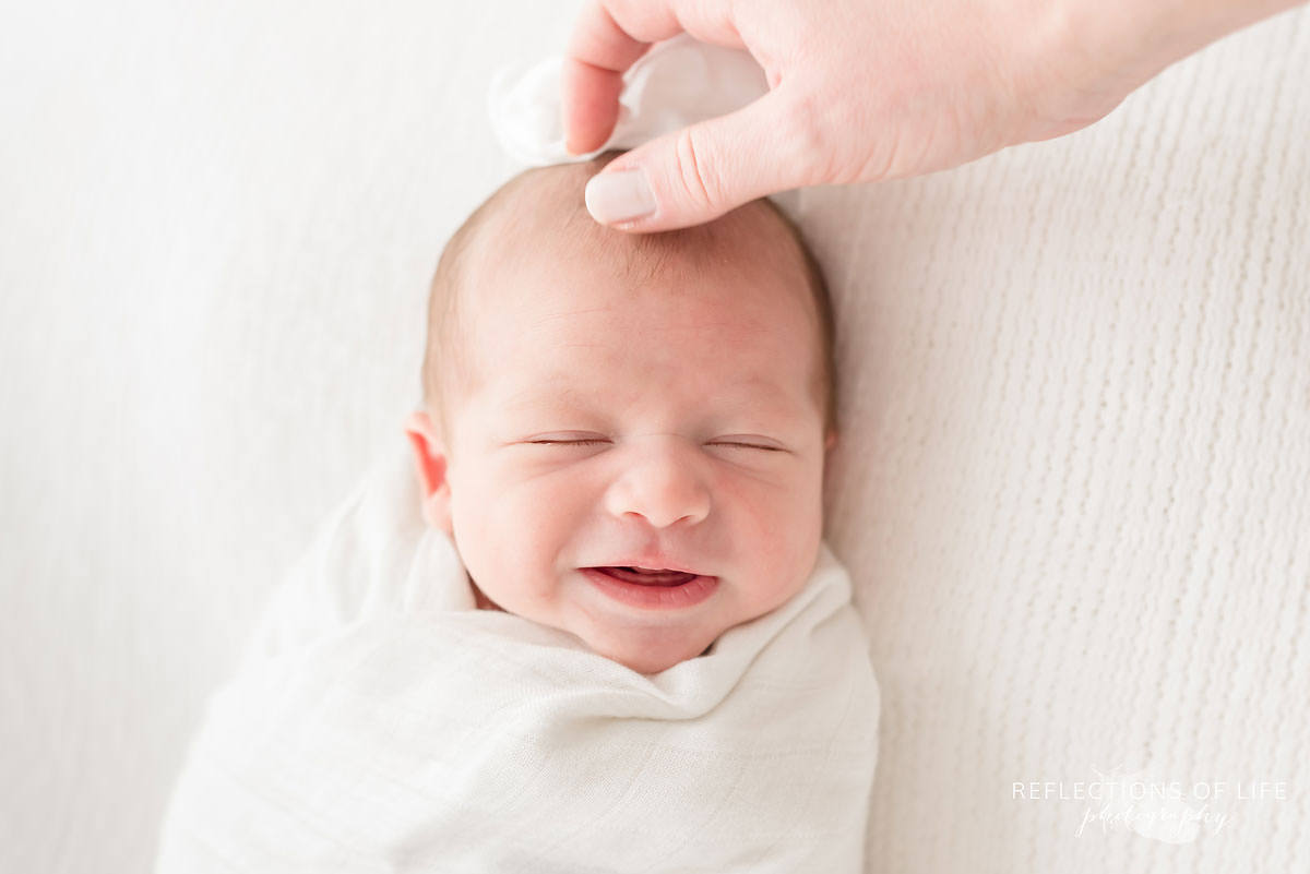 mother rubs her baby's head as he smiles in natural light studio