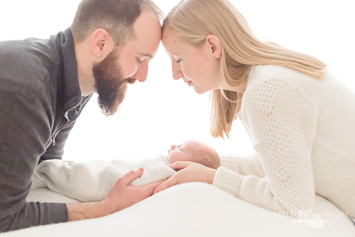 Mother and father lay over baby in natural light studio