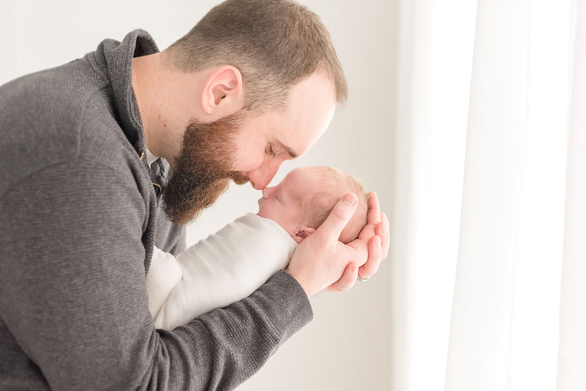 Father cradles baby's head in his hands in ontario