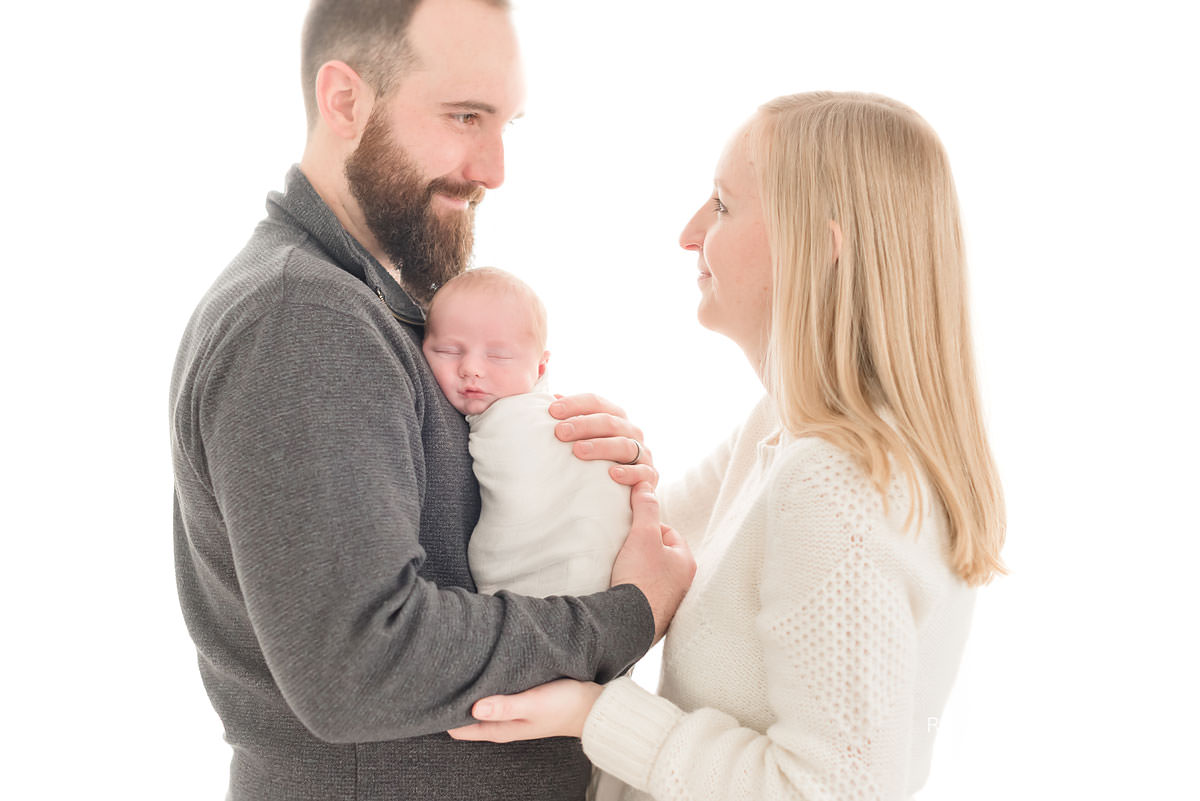Father holds baby to his chest as he looks at his beautiful wife