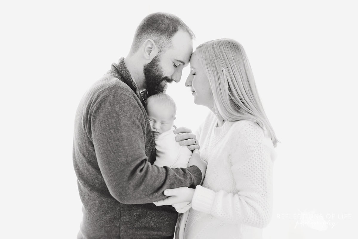 mom and dad cuddle their son in black and white