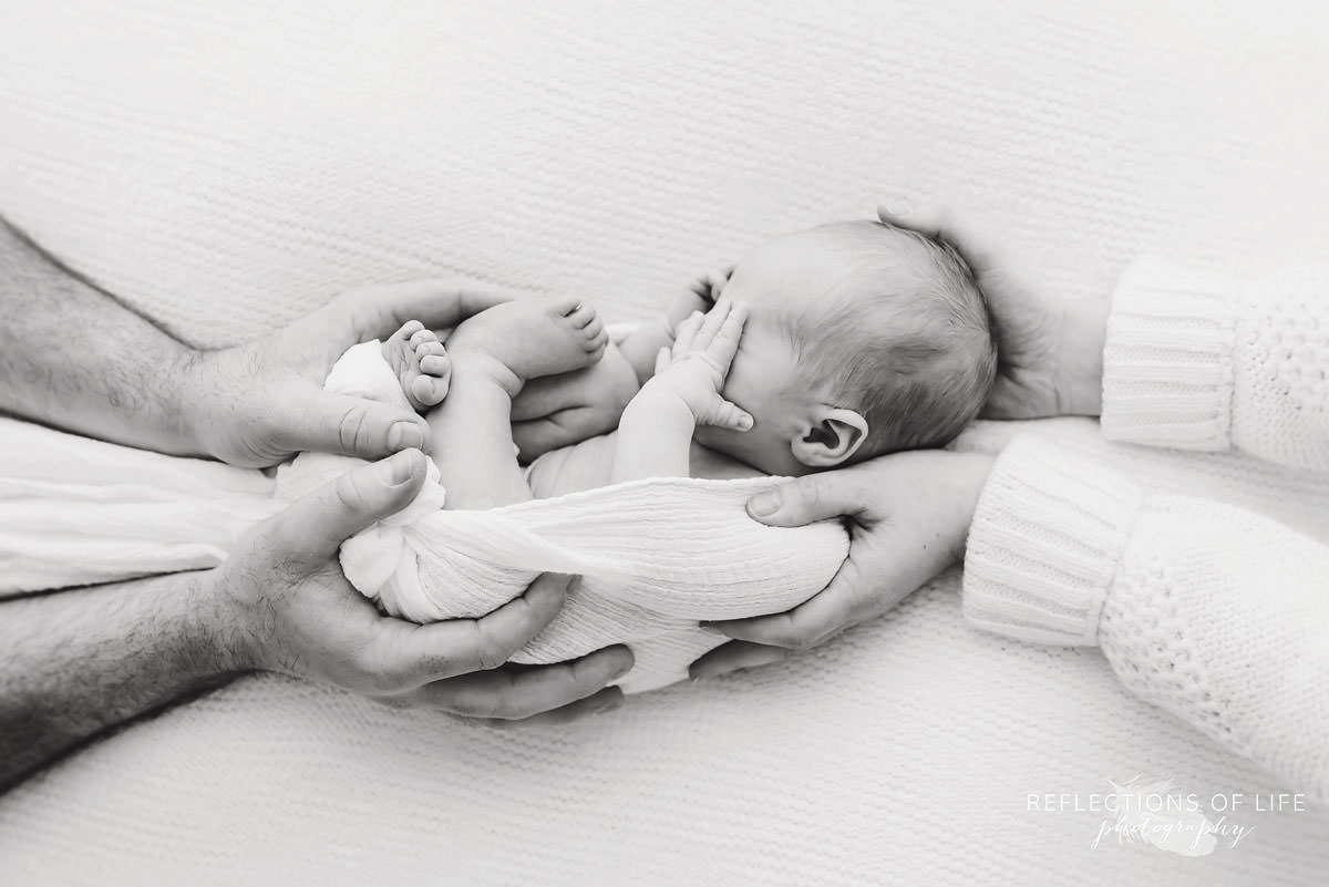 Mother and father hold their baby as he rubs his eyes in natural light studio