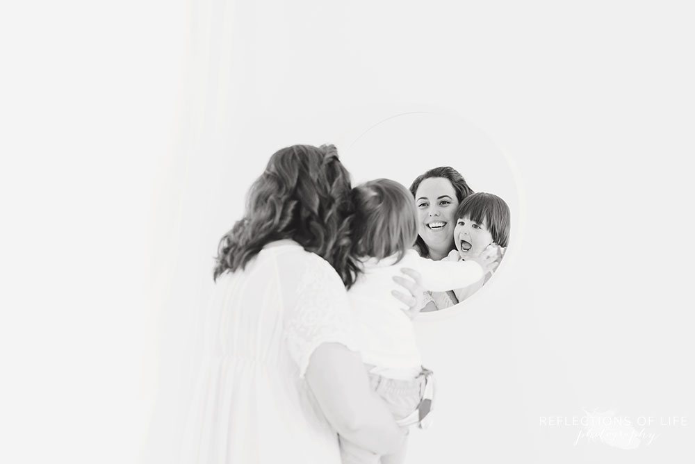 Baby and mom laugh while looking at reflection in the mirror