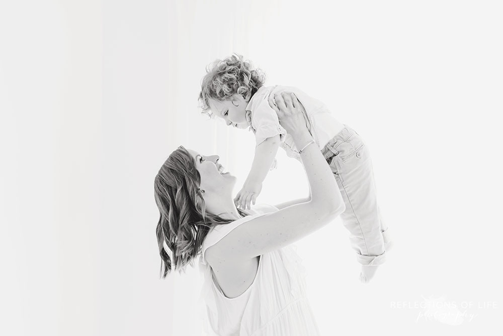 mama holds her baby up in the air in black and white in grimsby