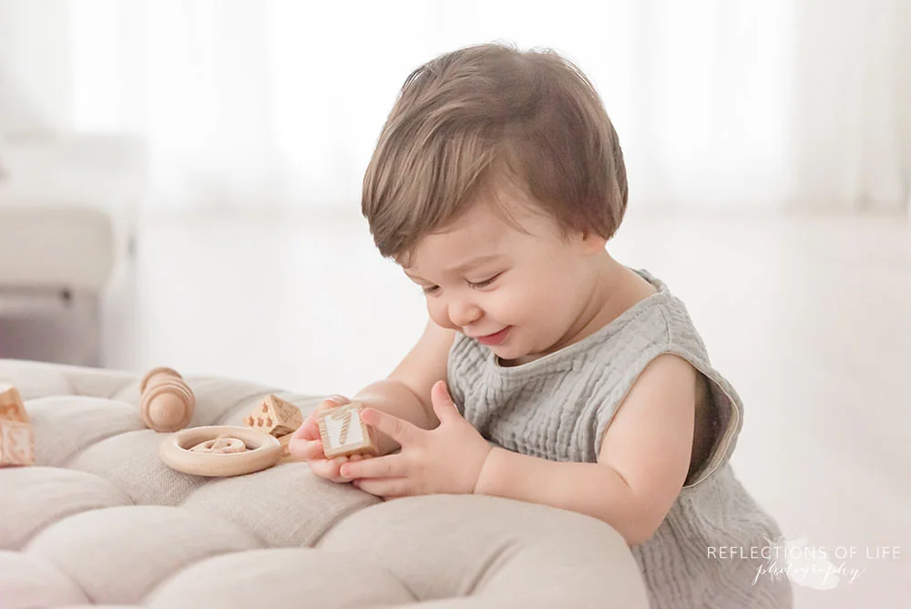 cute little boy smiles to himself while playing in natural light studio