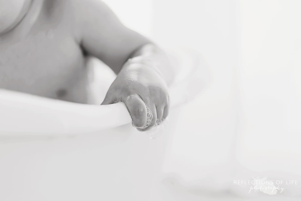 close up of baby grabbing the side of the tub in black and white