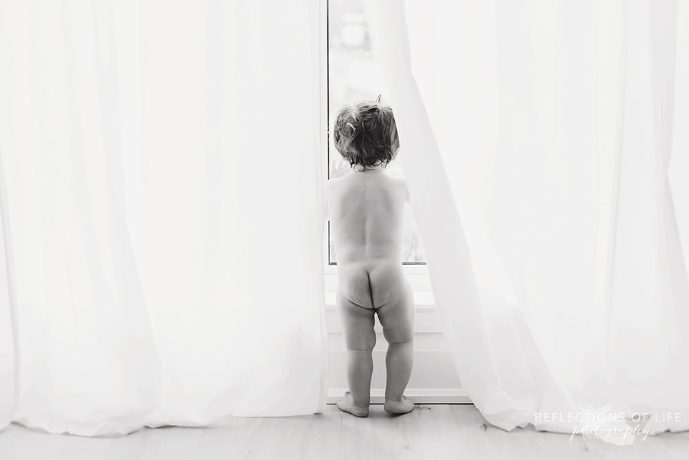 little boy looks out the window with his bum out in black and white