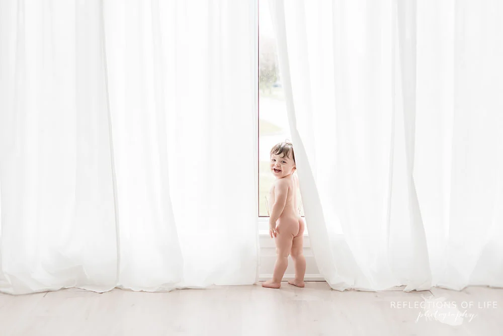 little boy smiles back at the camera as he looks out the window.jpg