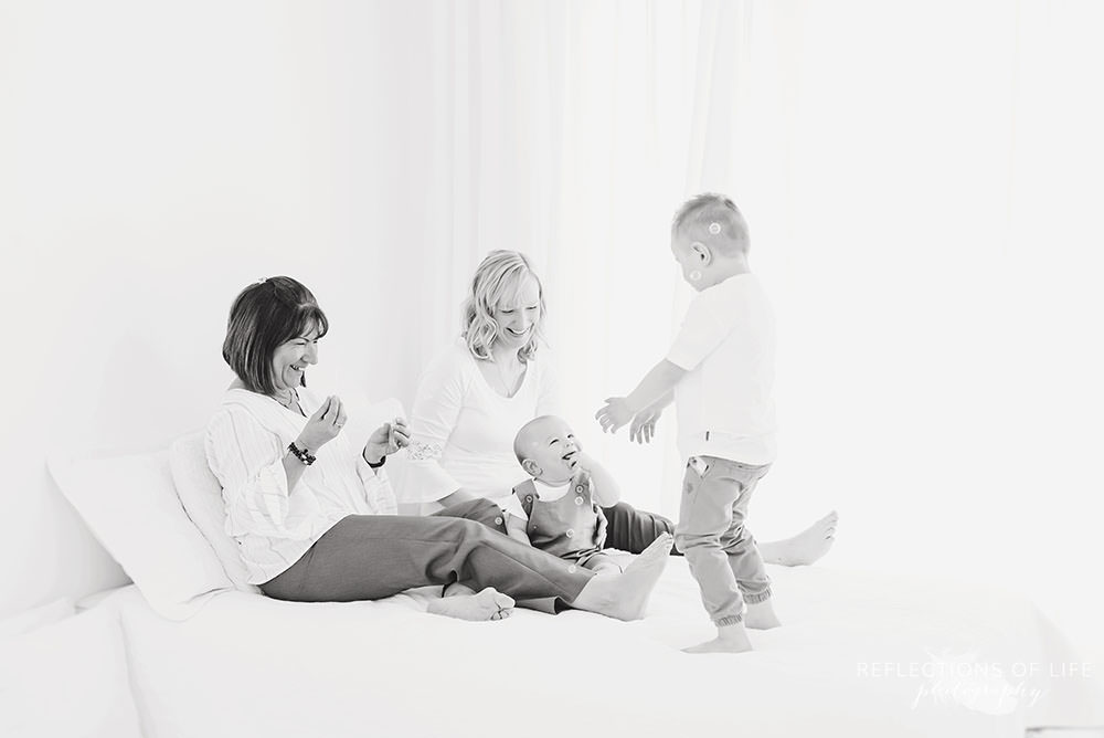 family of four play on a bed with mama and grandma