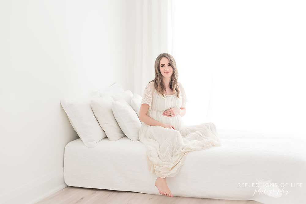 beautiful pregnant lady smiles as she sits on a bed in grismby