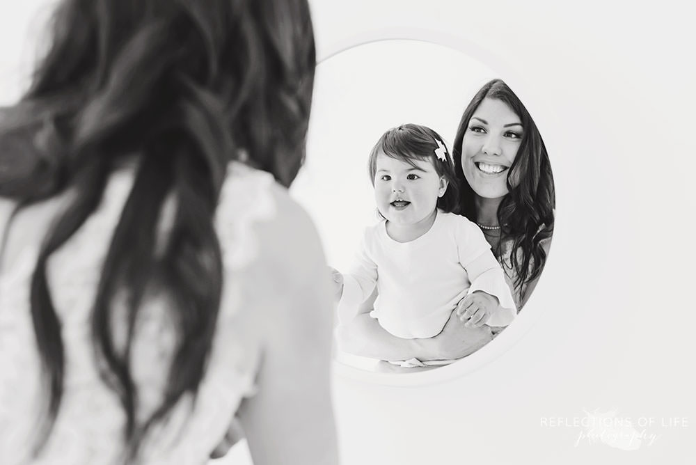 mama and daughter smile at the mirror together