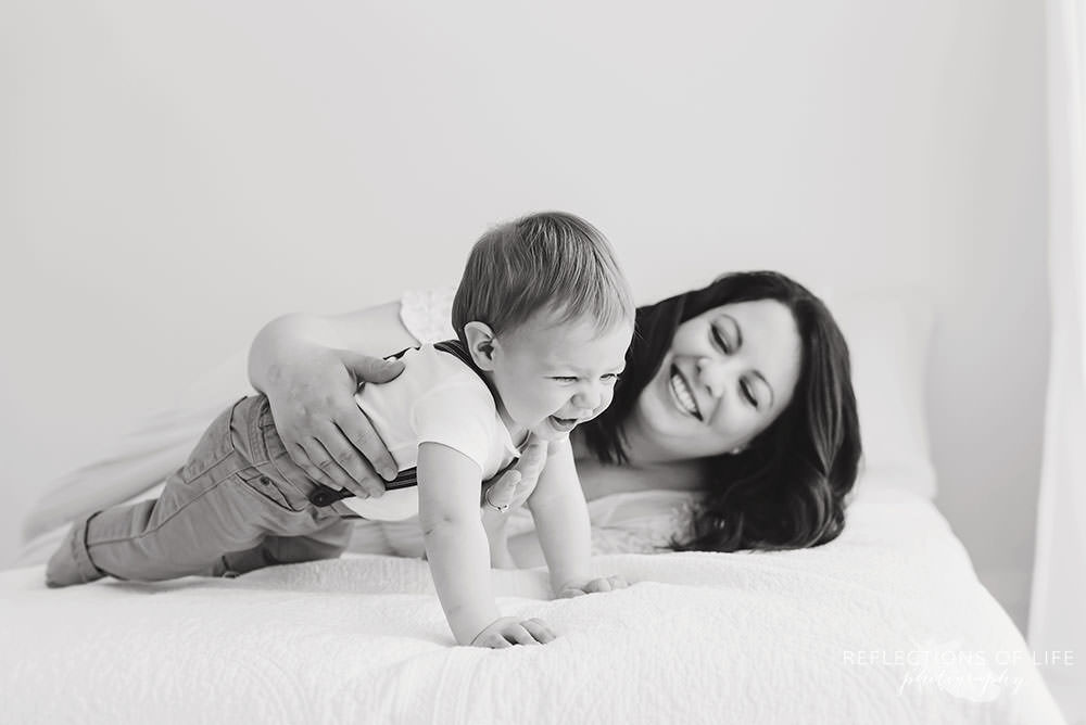 mama lays on bed and lets son crawl as they both laugh